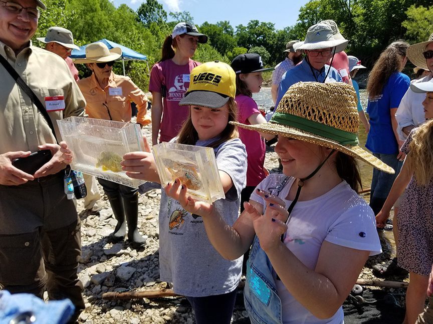 A young boy is holding a clear container with two fish in it.