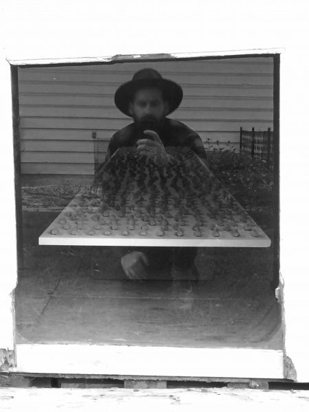 A man in a hat is taking a picture of himself in a mirror.
