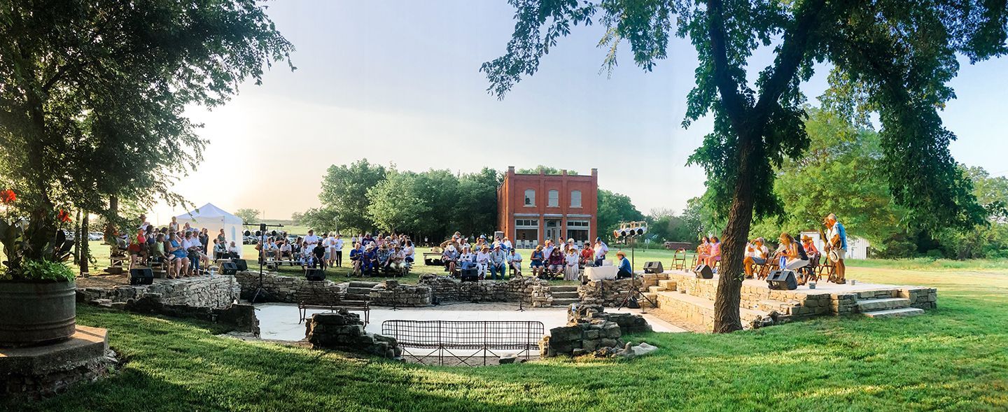A group of people are sitting on a stage in a park.