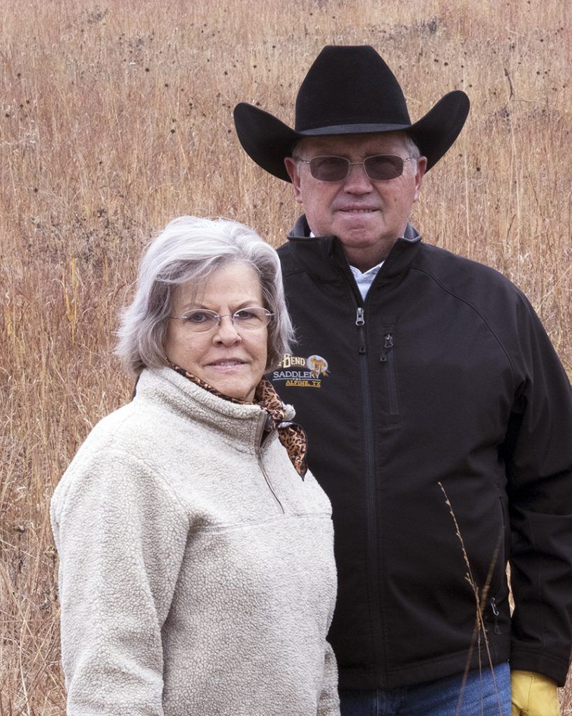 A man and a woman are posing for a picture in a field . the man is wearing a cowboy hat.