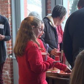 People at a gathering, girl in red sweater, others reaching for food.