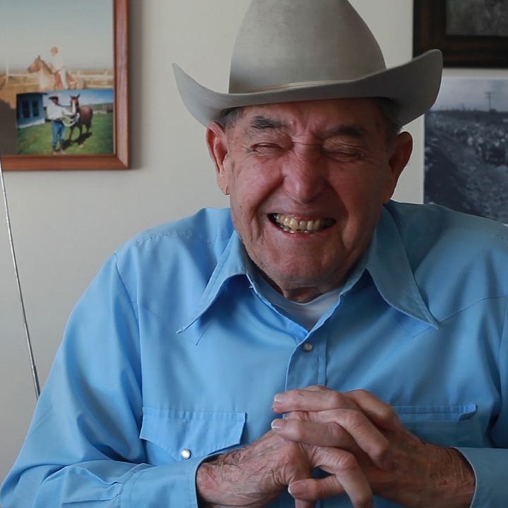 Elderly man in cowboy hat and blue shirt, laughing with eyes closed.