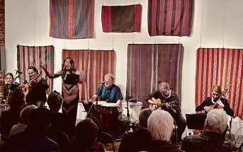 A band performs on stage, vocalist singing, audience watching, colorful tapestries backdrop.