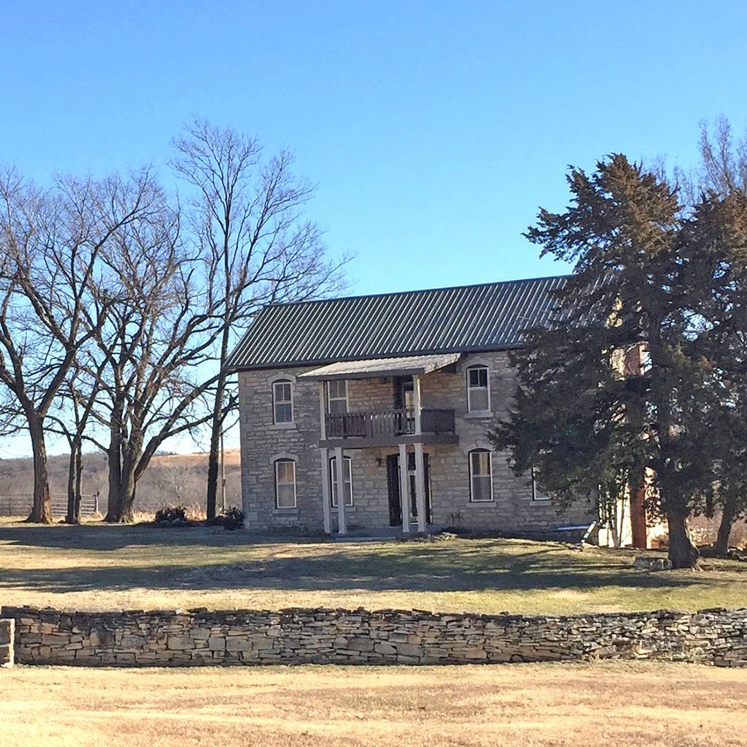 A large stone house is sitting in the middle of a field surrounded by trees.