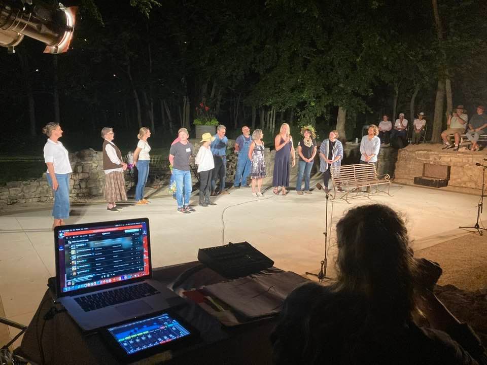 A group of people perform outside at night, with a soundboard in the foreground.