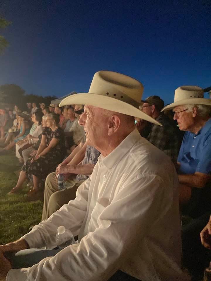 People in cowboy hats watching an outdoor event at dusk.