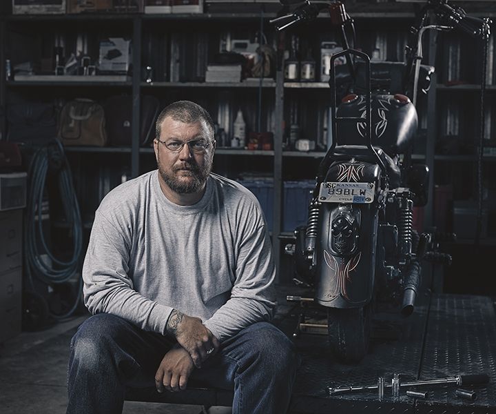 A man is sitting in front of a motorcycle in a garage.