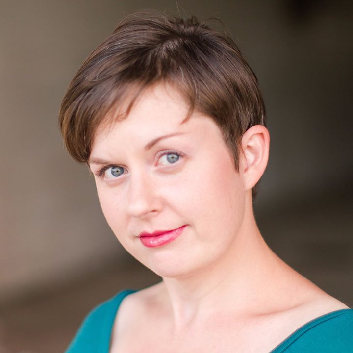 A woman with short brown hair is wearing a green shirt and smiling for the camera.