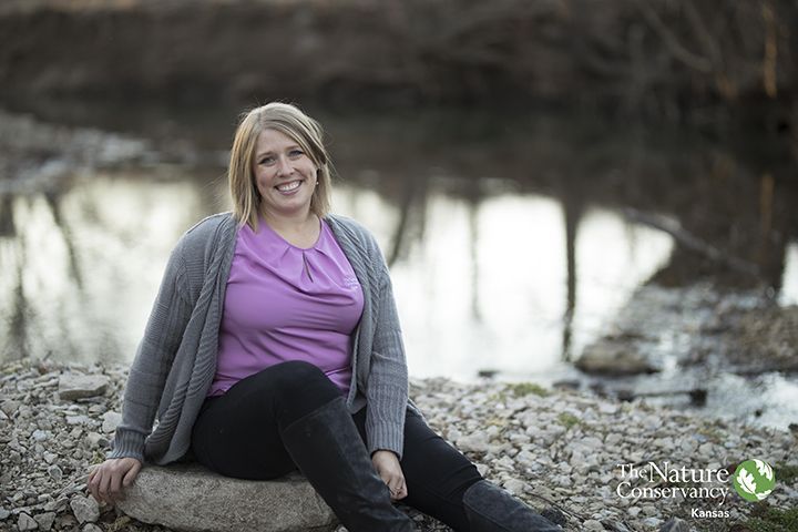 A woman is sitting on a rock next to a river.