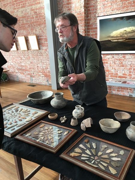 A man is standing in front of a table full of ancient artifacts.