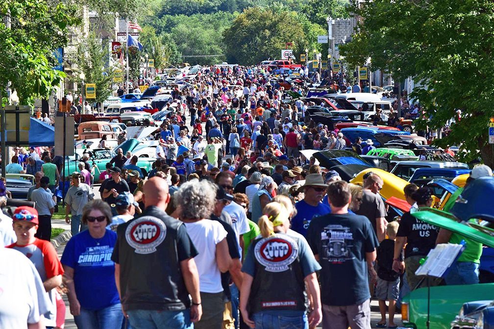 A crowd of people are walking down a street filled with cars.