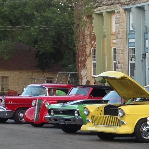 Classic cars line a street in front of colorful buildings; a car show.