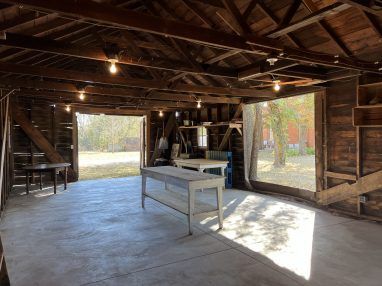 Open wooden garage with concrete floor. Two tables inside, natural light from openings.