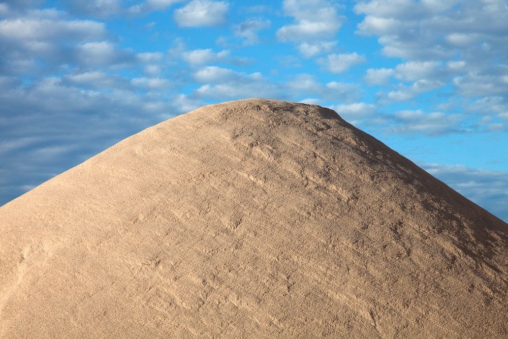 A large pile of sand against a blue sky with clouds