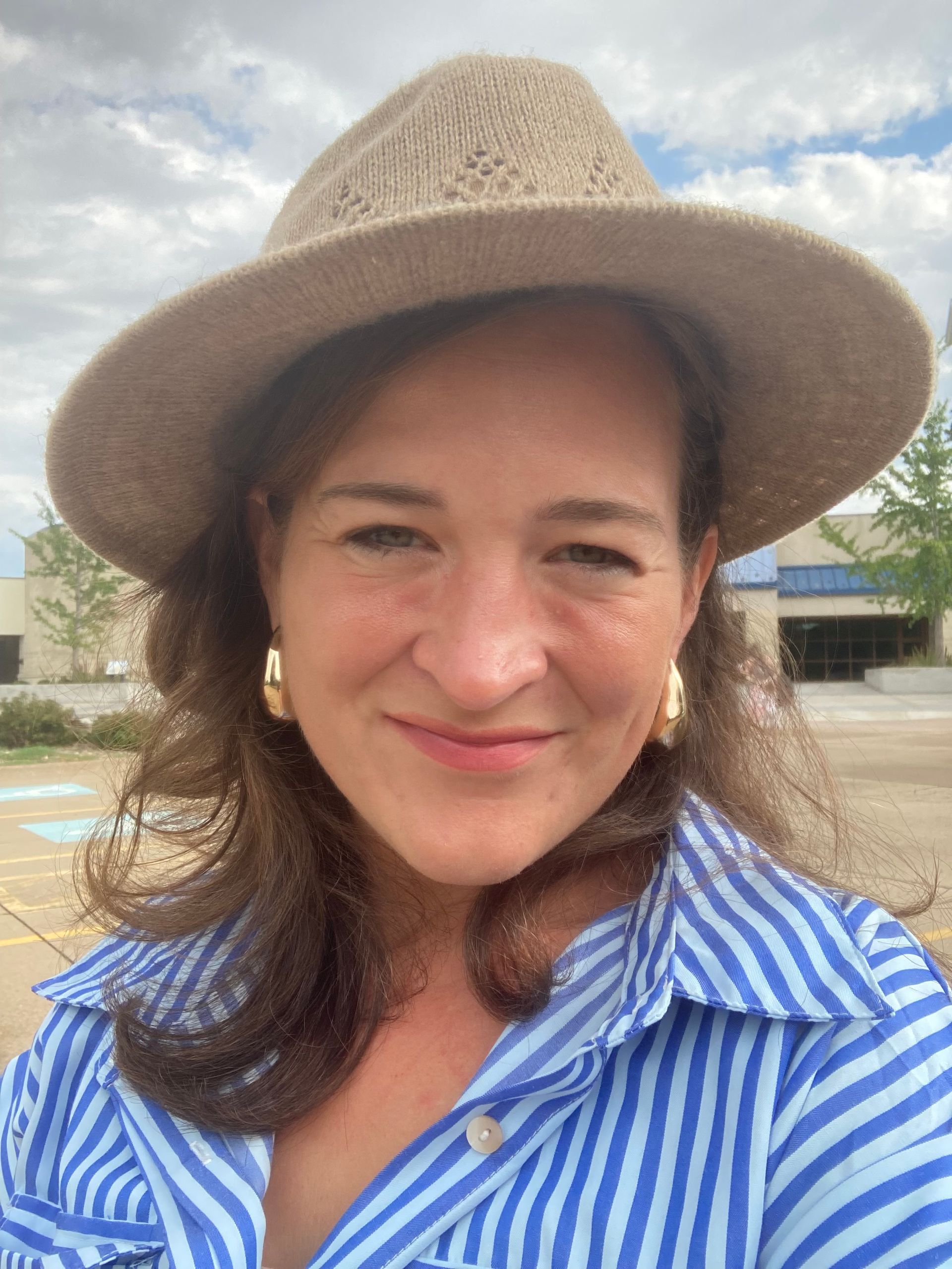 Woman in hat and striped shirt smiling, outdoors.