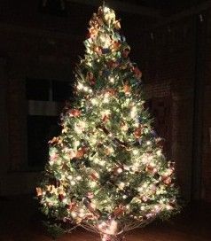 Christmas tree, lit with white lights and decorated with brown ornaments, in a dim room.