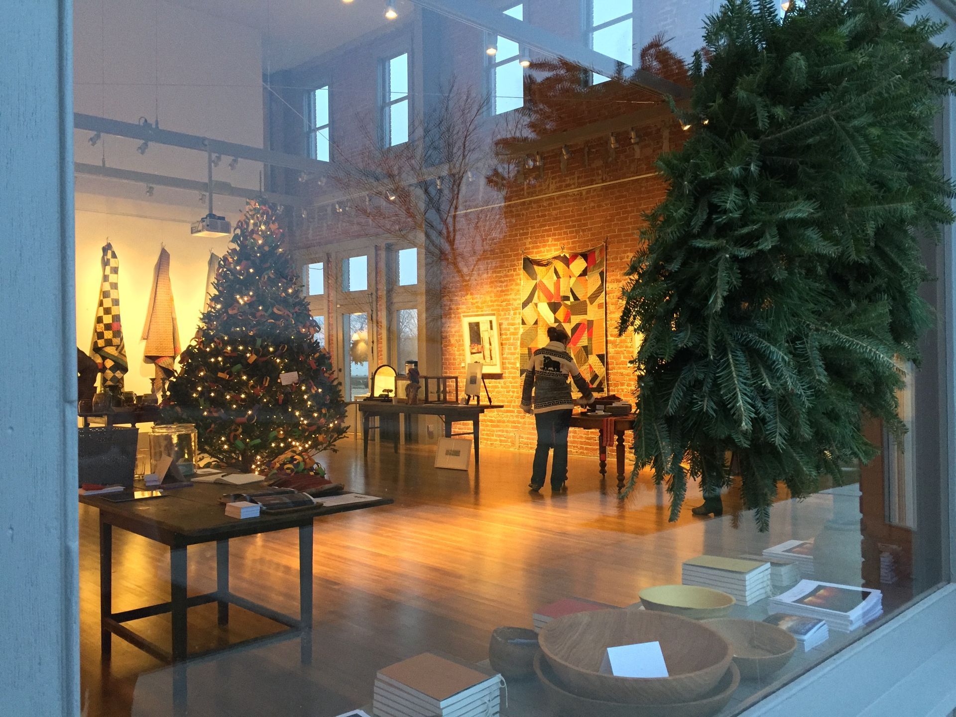 Storefront with Christmas trees and display tables, a person browsing art.