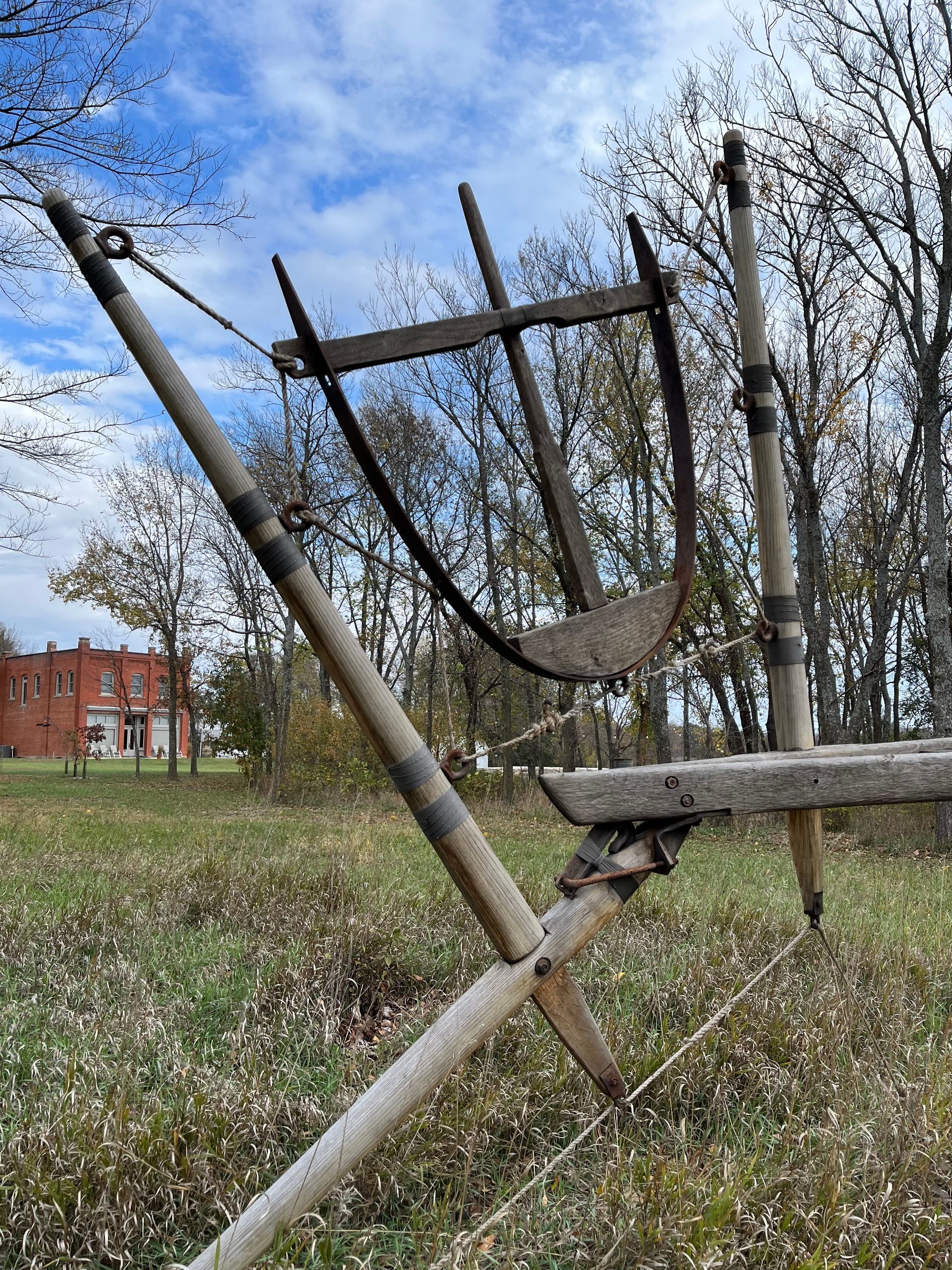 Man in cap smiles, working with wooden beams outdoors. In the background, is a red brick building.