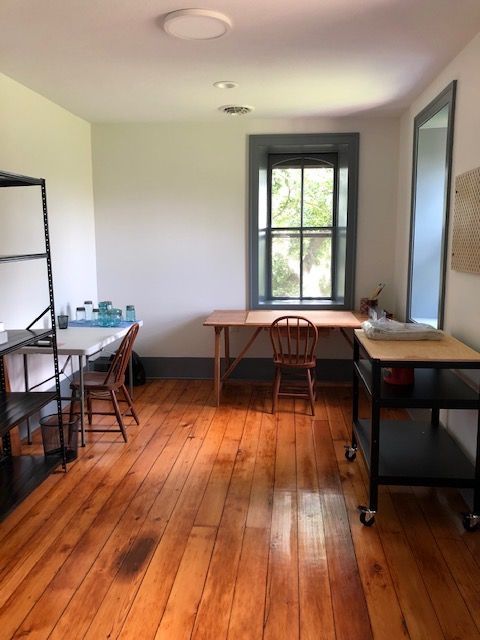 Room with wood floor, desks, chairs, and a window; white walls with grey trim.