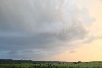 A cloudy sky over a field with trees in the foreground.