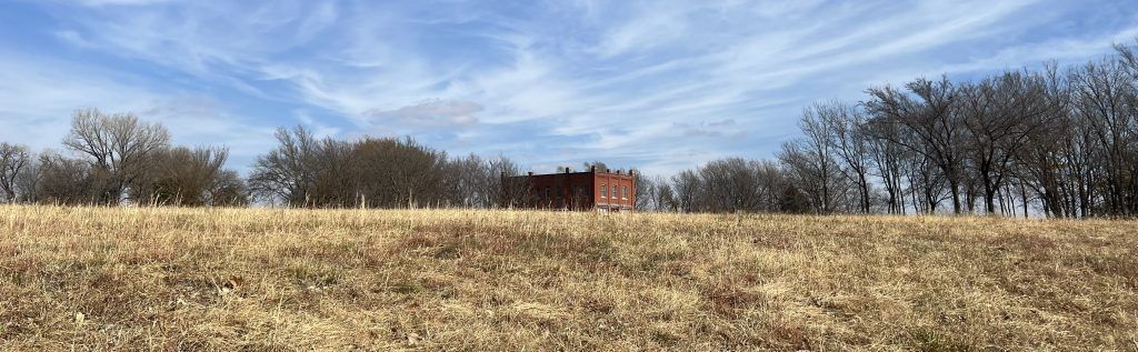 A winter field of soft golden grass, with the Volland Store (a brick building for art and community) on the horizon.