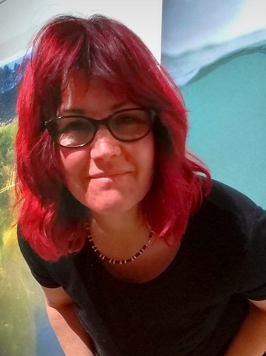 A woman with red hair wearing glasses and a black shirt
