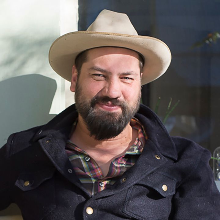 Man wearing a hat and jacket smiles.