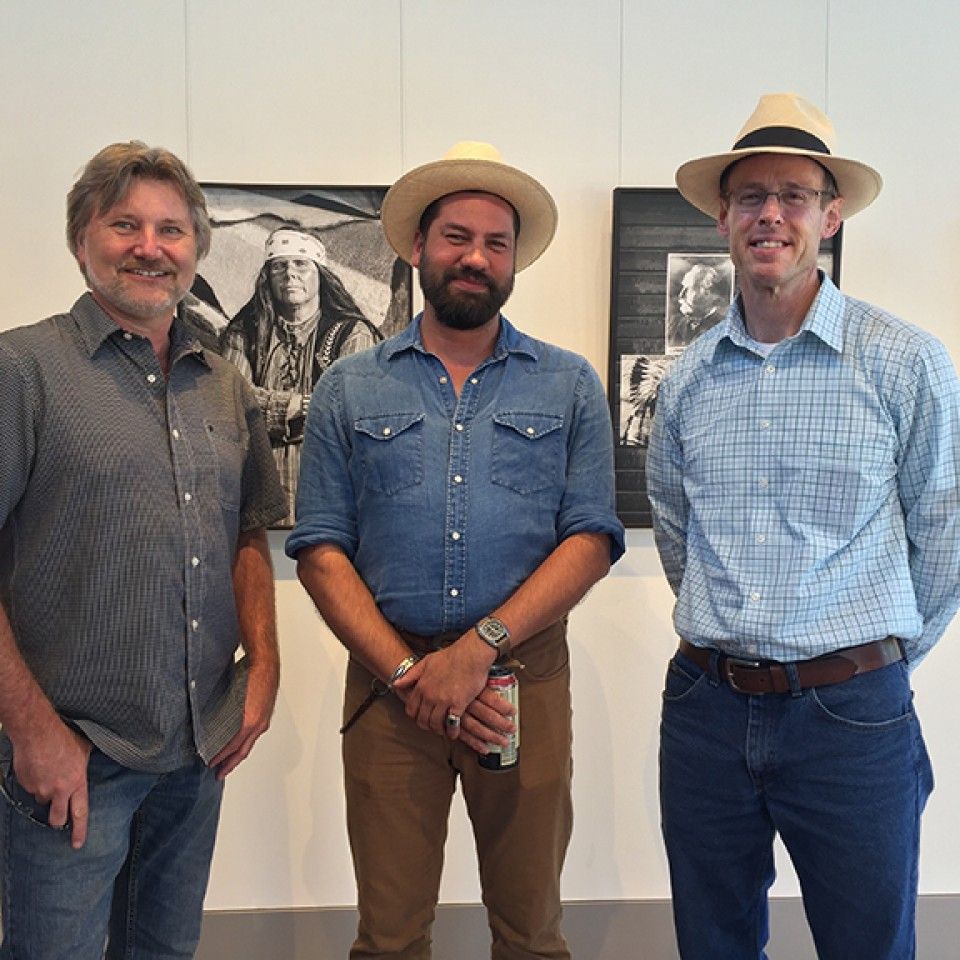 Three men are posing for a picture with one wearing a hat