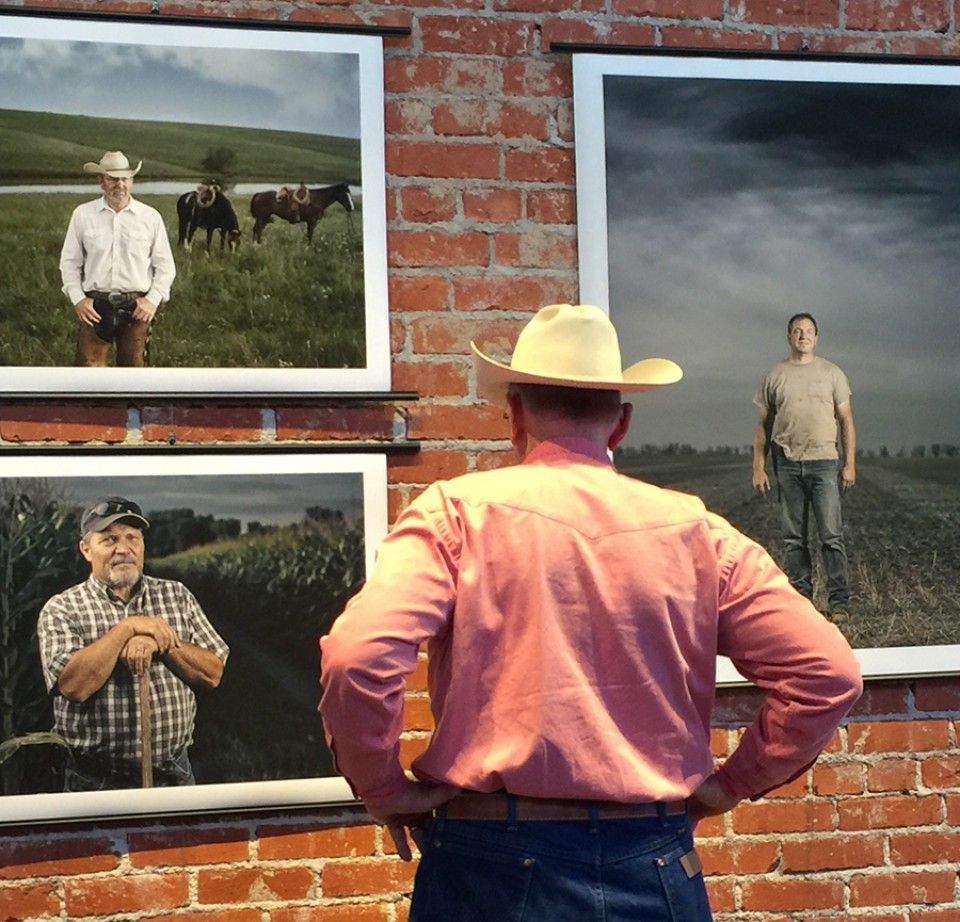 A man in a cowboy hat is looking at pictures on a brick wall