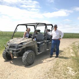 A man and two women pose by a camouflage ATV on a dirt road in a field.