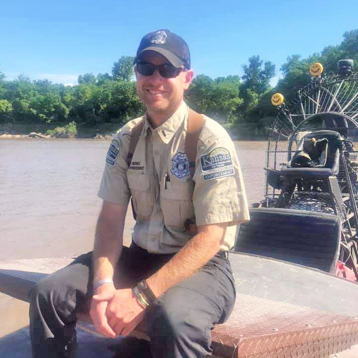 A man in a uniform is sitting on a boat near a body of water.