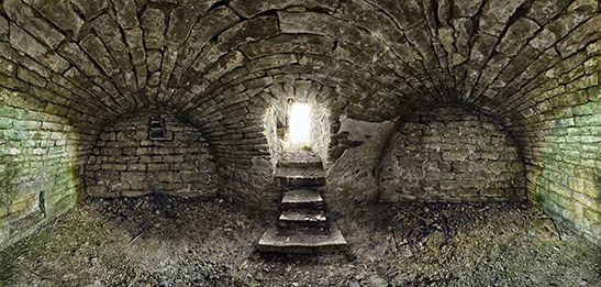 Stone arched tunnel with stairs leading to bright light.
