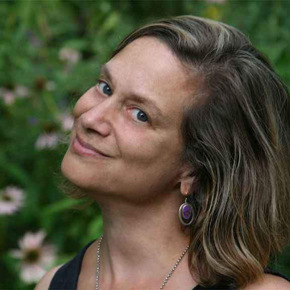 A woman wearing purple earrings and a necklace smiles for the camera