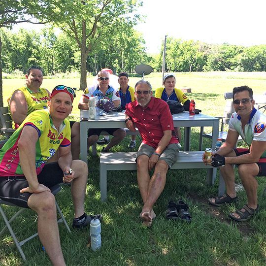A group of men are sitting at picnic tables in a park