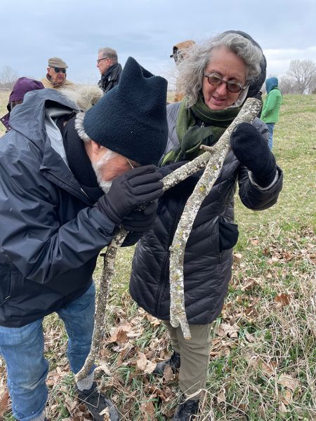 Two people examining a forked stick outdoors, others watch in a field.