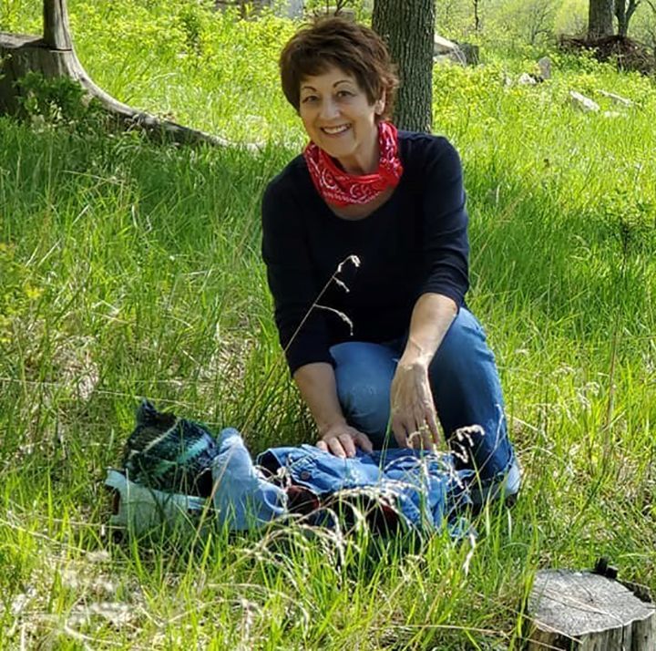 A woman wearing a red bandana is kneeling in the grass.