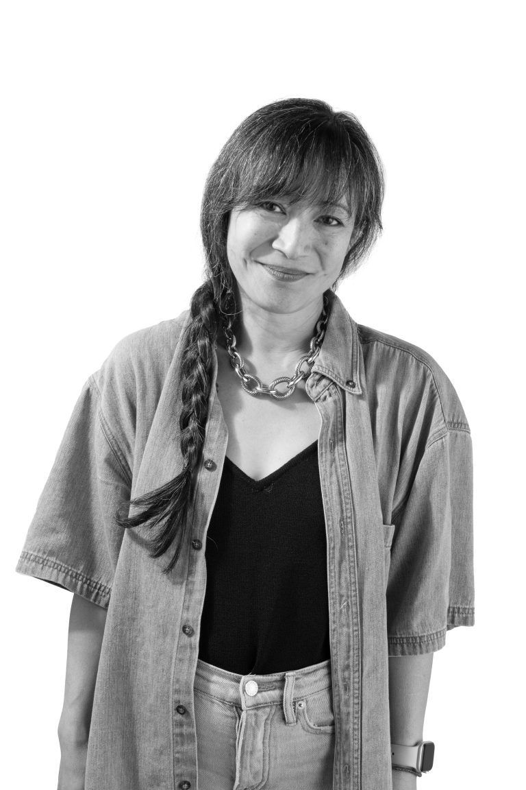 Woman with braided hair, smiling, wearing denim shirt and tank top.