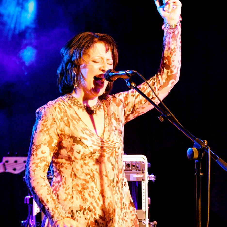 A woman singing into a microphone with her hand in the air