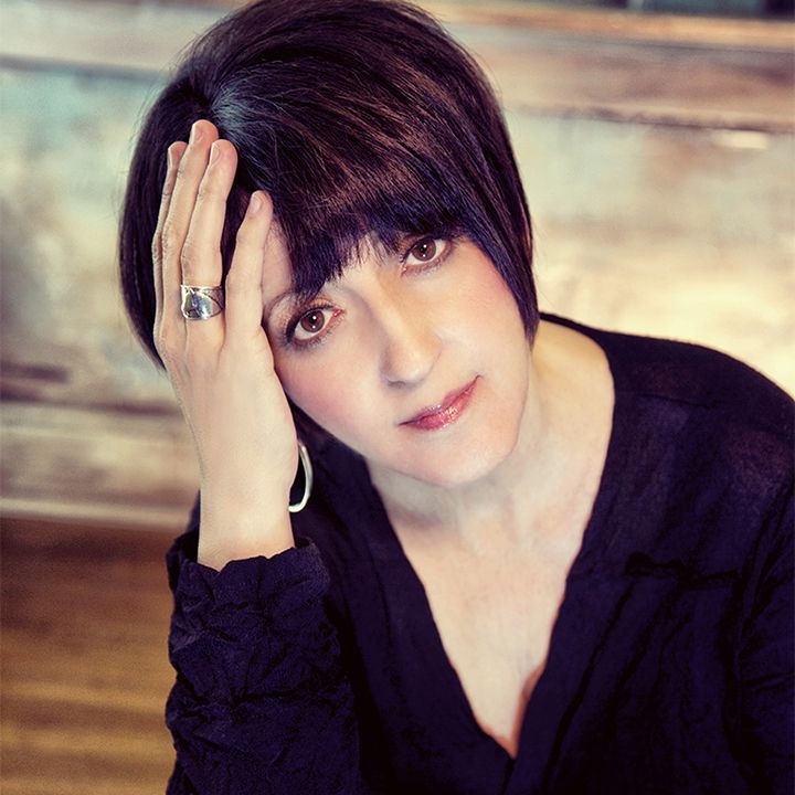 A woman with a ring on her finger holds her hand to her forehead