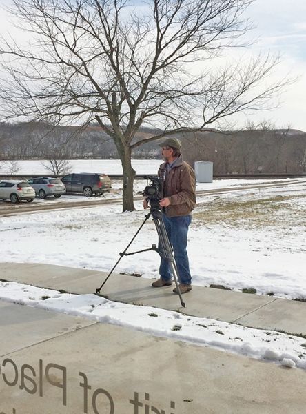 A man is standing on a sidewalk in the snow holding a camera