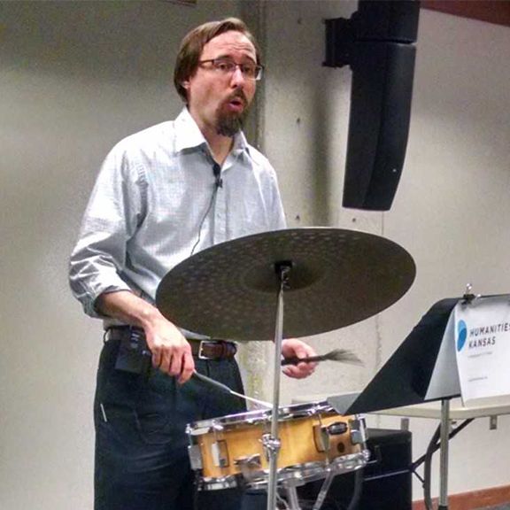 A man playing drums in front of a sign that says humante