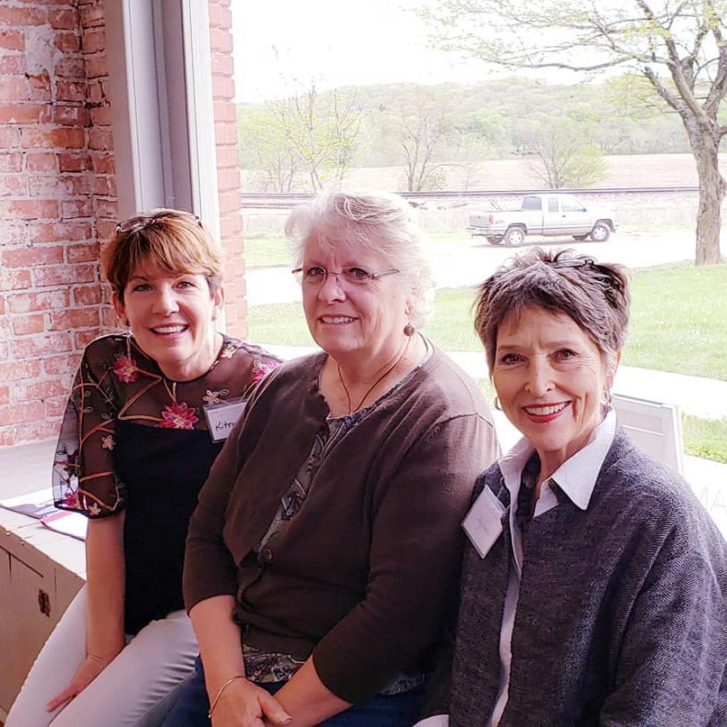 Three women are sitting in front of a window and smiling