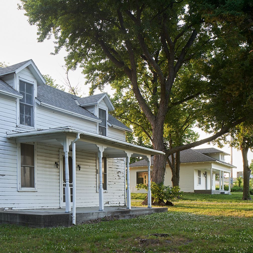 A white house with a porch and a tree in front of it