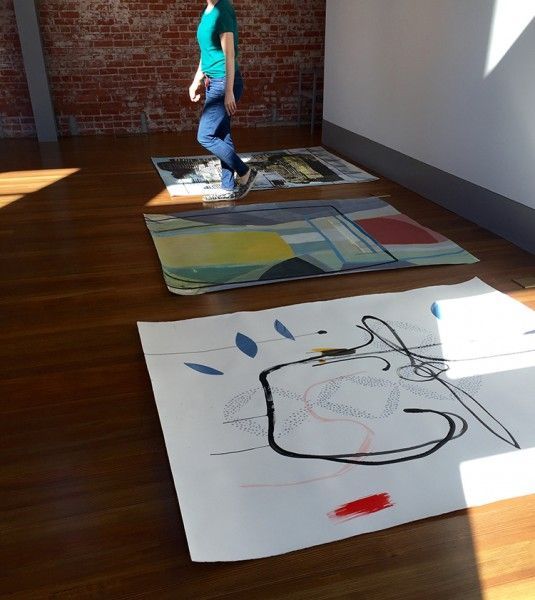 A woman in a green shirt is walking in a room with paintings on the floor