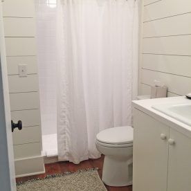 Small white bathroom with shiplap walls, white fixtures, and a gray rug.