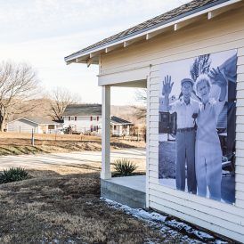 A black and white mural of a couple waving on a building's side; other houses are visible in the background.
