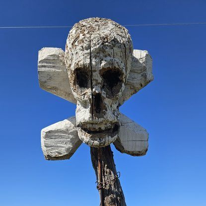 Wooden skull and crossbones sculpture against a bright blue sky.
