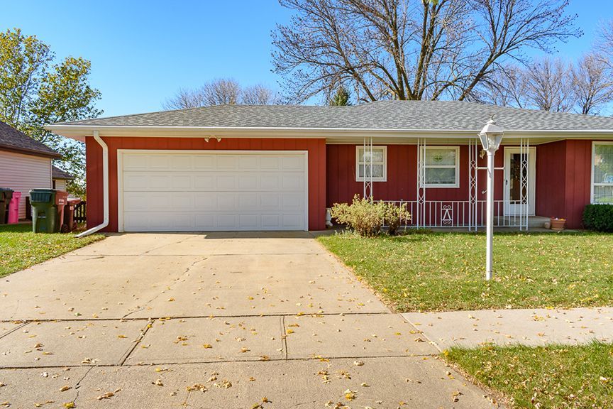 Red ranch-style house with a white garage door and front porch, with a concrete driveway and green lawn.