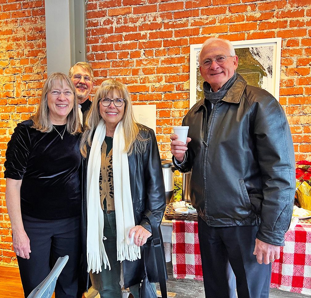Two women, two men smiling at the camera in front of the refreshment table