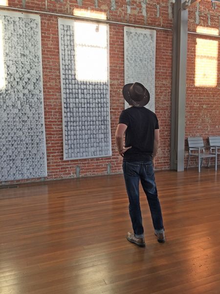A man in a hat is standing in a room looking at a brick wall.